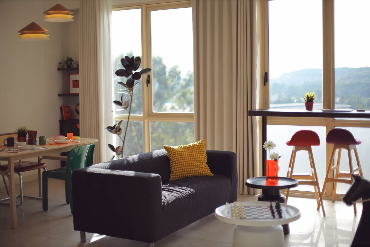 Living and dining space of a third RoomGuru-managed two-bedroom at Afiniti in Medini, with a breakfast bar at the window and hills beyond