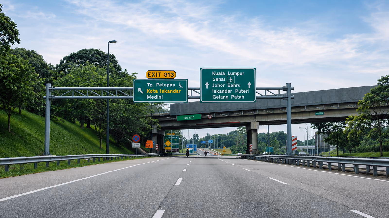Overhead expressway signs on the approach to Medini. The left sign, marked Exit 313, points to Tanjung Pelepas, Kota Iskandar and Medini. The separate sign beside it points straight ahead for Kuala Lumpur, Senai airport, Johor Bahru, Iskandar Puteri and Gelang Patah.